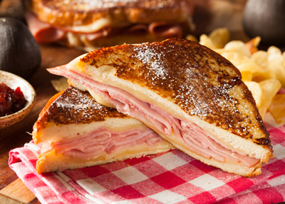 grilled ham and cheese sandwich sliced in half with crispy chips on a checkered napkin serving two delicious flavors